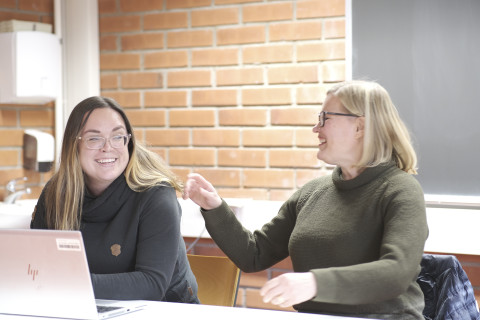 Kaksi naista keskustelevat seminaarisalissa innostuneesti.