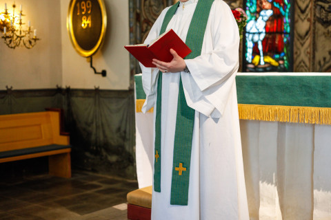 Pappi kirkon alttarilla raamattu kädessä.