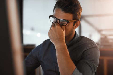 Mies hieroo väsyneitä silmiään toimistossa.