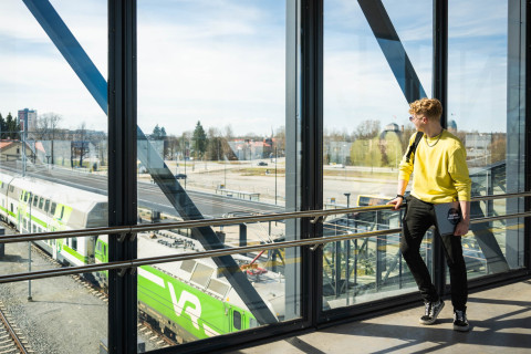 Keltapaitainen henkilö Joensuun juna-aseman ylikulkusillalla katsoo raiteilla olevaa junaa