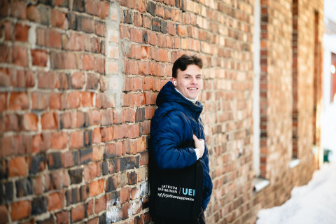 Mies nojaa seinään ja hymyilee kameralle talvella