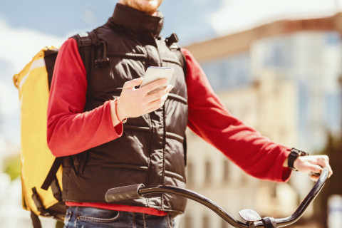 Ruokalähetti katsoo kännykkää pyörän selässä.