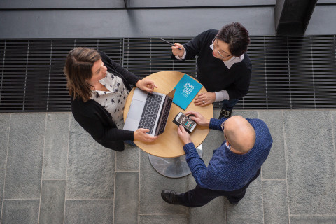 Kolme henkilöä neuvottelee pöydän ympärillä.