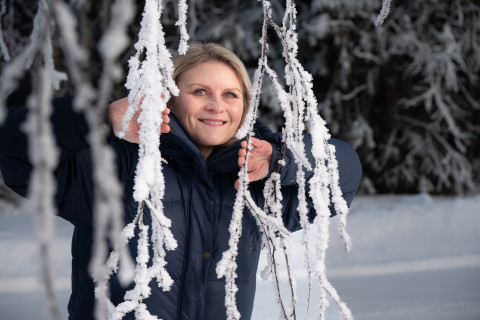 Opiskelija Tanja Nikkilä kurkkaamassa huurteisten oksien välistä talvisessa maisemassa
