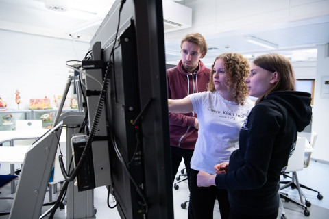 Kolme henkilöä katsoo tietoja isolta näytöltä