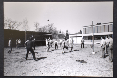 Miehiä pelaamassa lentopalloa ulkona hiekkakentällä.