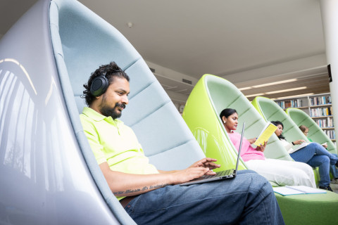 Opiskelijoita lukemassa kirjaa kuplatuoleissa; Students reading a book in bubble chairs.