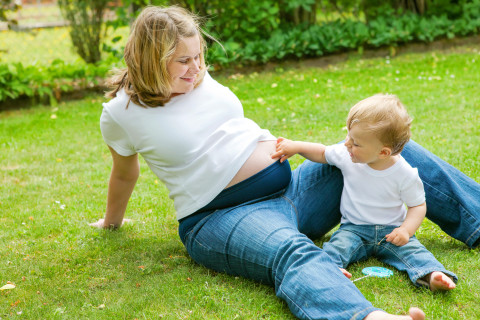 Pregnant mother and toddler sitting on lawn.