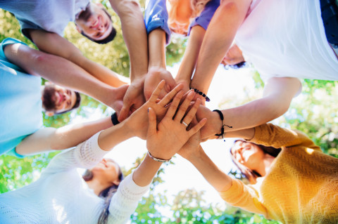 A group of people standing in a circle holding hands on top of each others&#039; hands.