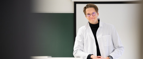 aineenopettajaopiskelija luokkahuoneen edessä laboratoriotakki yllään