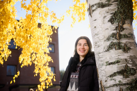 Student smiling on outside next to a birch