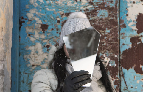 Henkilö pitää peilin palaa kasvojensa edessä