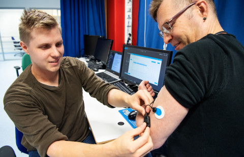 Tutkija asettaa anturia koehenkilön käsivarteen