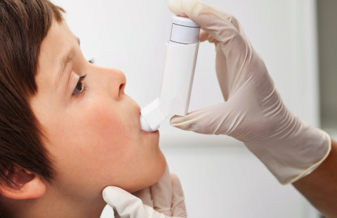 Aikuinen auttaa lasta käyttämään astmapiippua.