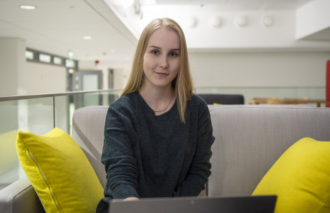 naisopiskelija istumassa itseopiskelutilan sohvalla