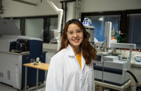 Young woman in a lab coat smiling, laboratory in the background.
