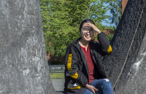 Young woman sitting outside, sun is shining brightly and she is shading her eyes with one hand.