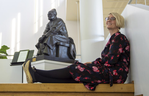 Nainen istuu lattialla runonlaulaja-patsaan vierellä.