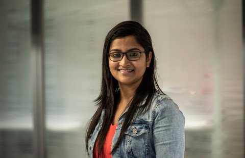 Young woman with dark long hair and glasses smiling for the camera.