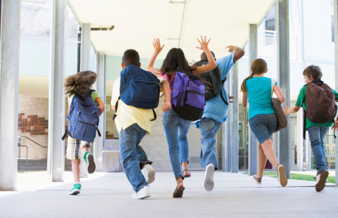 koululaiset juoksevat koulun käytävällä reput selässä