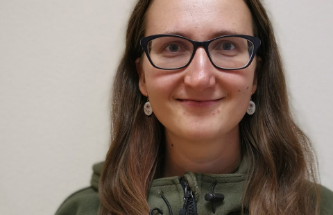 Young woman with glasses and long hair looking straight to the camera and smiling.