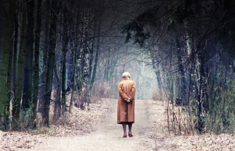 Vanha nainen kävelee metsätiellä.