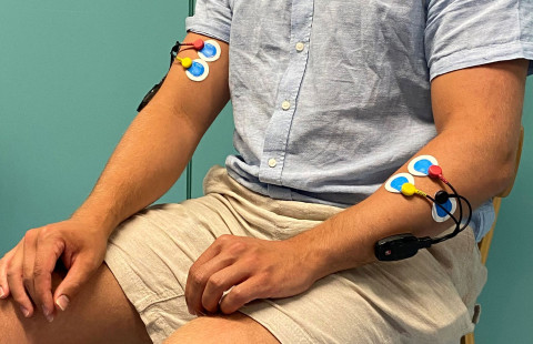 A person sitting down and wearing sensors on their arms