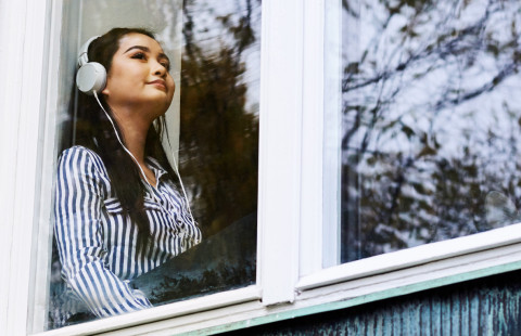 Opiskelija istuu ikkunan ääressä kuulokkeet päässä.