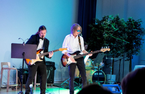 Kaksi nuorta miestä soittimien kanssa etualalla, kolmas taustalla