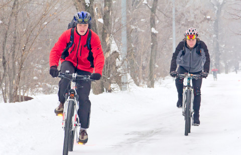 Kaksi henkilöä polkee polkupyörällä talvista tietä.