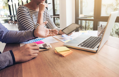 Kaksi henkilöä keskustelee kannettavan tietokoneen äärellä.