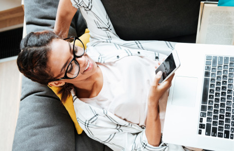 Nainen työskentelee kannettavalla tietokoneella ja matkapuhelimella.