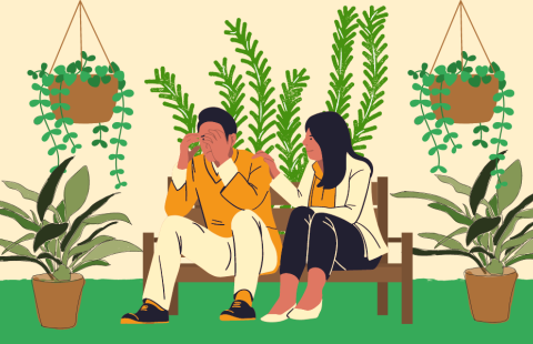 Kaksi henkilöä istuu penkillä viherkasvien ympäröimänä. Henkilöistä toinen peittää kasvojaan käsiin ja toinen pitää kättään toisen olkapäällä.