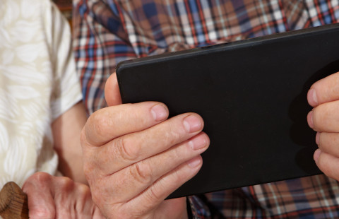 Iäkäs ihminen pitelee tablet-tietokonetta käsissään.