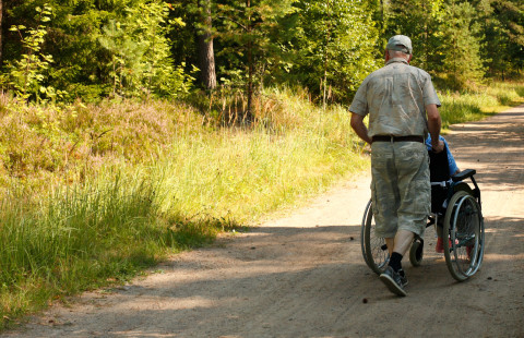 Mies työntää pyörätuolia hiekkatiellä.