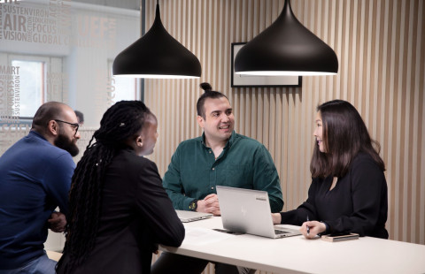 Neljä henkilöä neuvottelee pöydän äärellä aulatilassa.