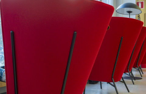 Punaisia nojatuoleja Joensuun kampuskirjastossa. Etualalla olevassa tuolissa istuu henkiläö, joka on riisunut kengät ja nostanut jalat ylös.