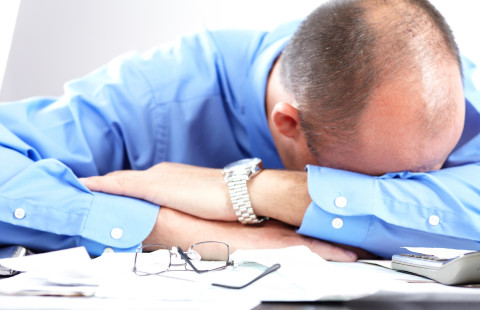 Mies nojaa pöydällä oleviin käsivarsiin.