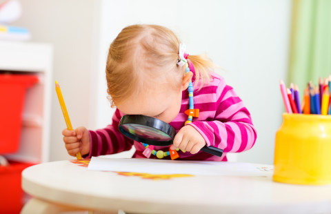 Lapsi tarkastelee suurennuslasilla piirrostaan. 