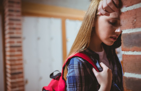 Nuori nojaa otsaansa tiiliseinää vasten.