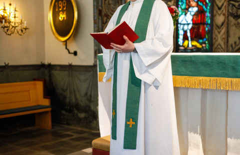 Pappi kirkon alttarilla raamattu kädessä.