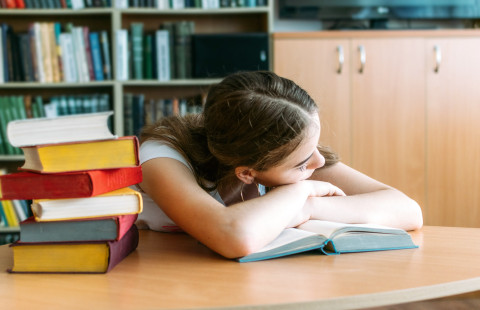 Oppilas haaveilee kirjapinon vieressä.