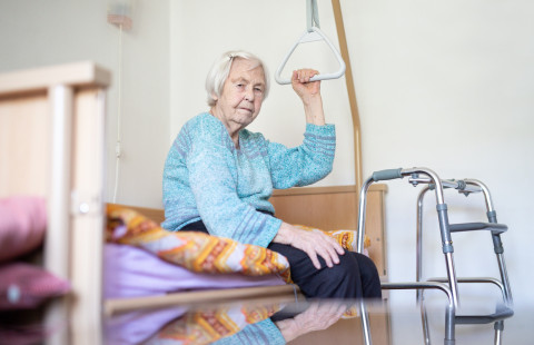 Ikäihminen istuu sängyssä pitäen kiinni kohottautumistelineen kahvasta.