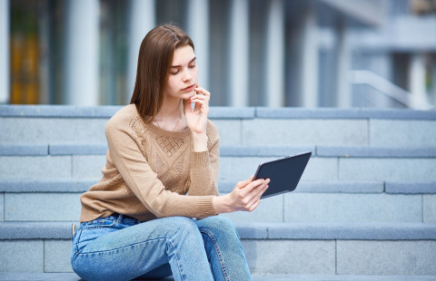 Nuori henkilö istuu kiviportailla tabletti kädessään.