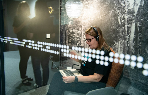 Nainen käyttää tietokonetta kuulokkeet päässä.