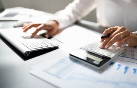 Kädet tietokoneen ja laskimen näppäimistöillä.