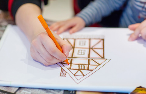 Kädet piirtävät taloa paperille.