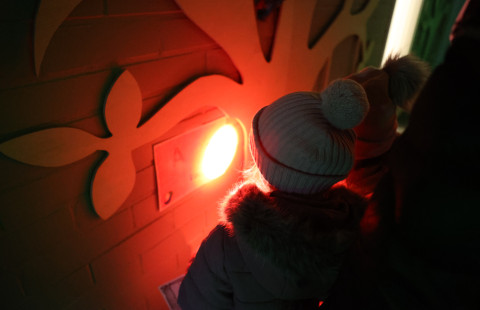 Children in winter clothing observe a bright red light on a decorated wall in a dimly lit environment