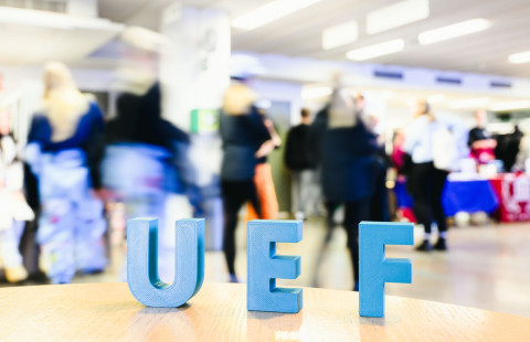 UEF -kirjaimet pöydällä taustallaan Hae yliopistoon -päivien ihmisvirtaa
