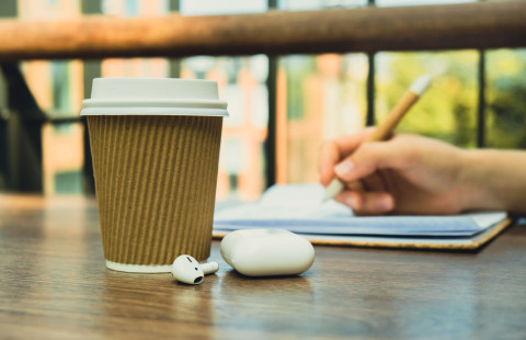 Kierrätyspahvista tehty kahvimuki kirjoituslehtiön päällä olevan käden edessä.